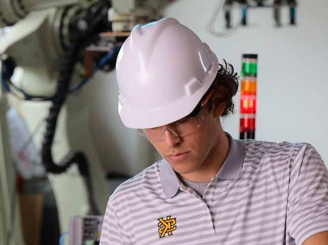 Student wearing safety goggles and hard hat focusing on project